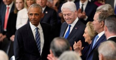 Barack Obama stands next to Bill Clinton and looks into a crowd of people.