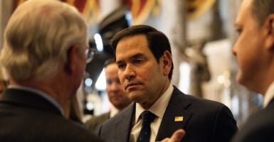 Marco Rubio stands and listens in a crowd of people.