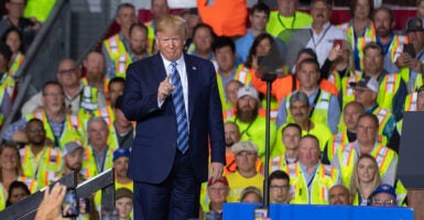 Donald Trump in a blue suit gestures in front of Shell workers