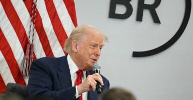 Donald Trump chats with a crowd of people while sitting down and holding a microphone in his right hand.