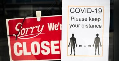 A sign that says the store is closed hangs in the window along with another sign telling people to practice social distancing.