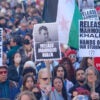 crowds of protesters, young and old, hold up a Palestinian flag and placards saying Release Mahmoud Khalil