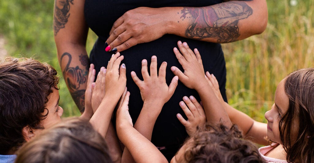 Black woman puts hand over her pregnant belly as her two sets of twins also place their hands there