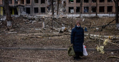 A woman in black stands in front of a building destroyed by bombing in Ukraine