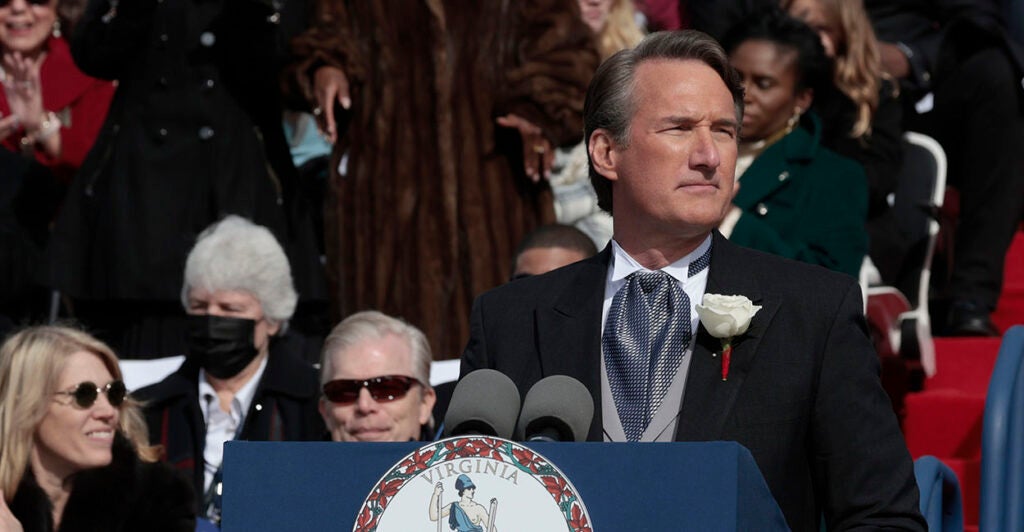 Glenn Youngkin in a suit stands behind a podium with "Virginia" on it