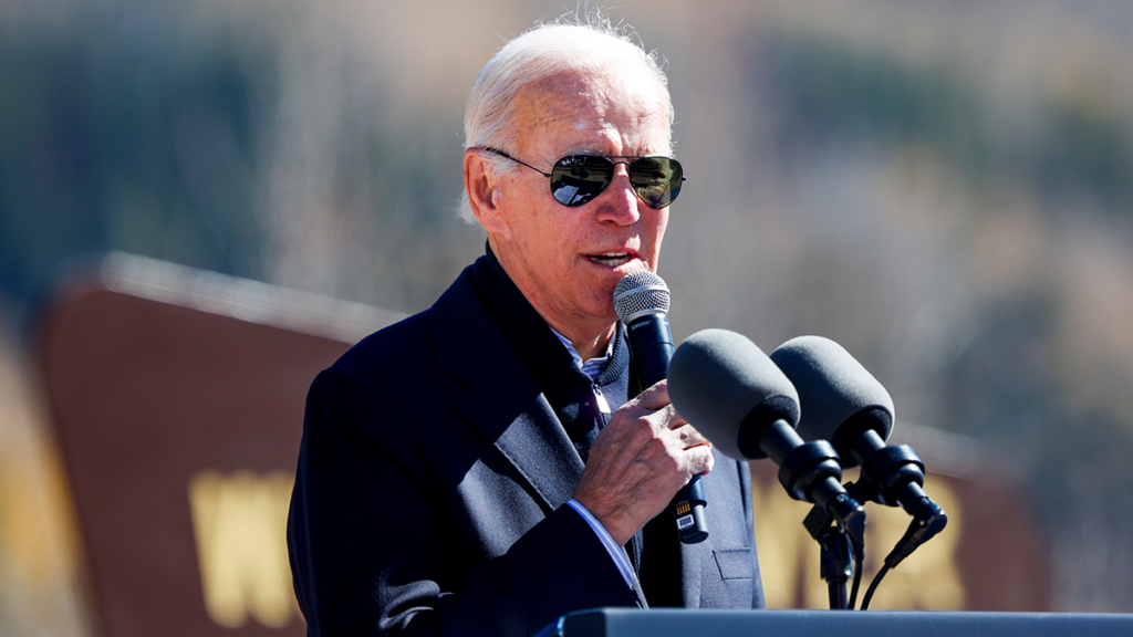 President Joe Biden holds a microphone and speaks in front of other microphones